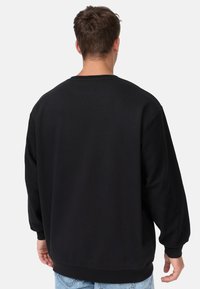 Schwarzes, übergroßes Sweatshirt mit langen Ärmeln, gerippten Bündchen und Rundhalsausschnitt. Glatte Textur, keine sichtbaren Muster, von hinten gezeigt.