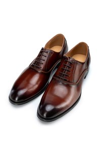 Zapatos de vestir de cuero marrón con un acabado pulido, punta redondeada, cierre de cuerda y costura decorativa a lo largo de la costura.