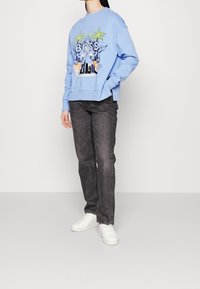 Světle modrá mikina s grafickou potiskem zahrnujícím palmy a slovo "BOSS". Doplněná o tmavě šedé džíny a bílé tenisky.