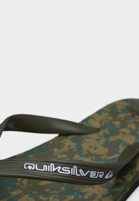 Σαγιονάρα με λουριά σε σκουροπράσινο χρώμα και πάτο με καμουφλάζ σχέδιο, με το λευκό λογότυπο "Quiksilver" στο λουρί.