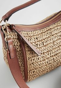 Sac en paille tissé avec des accents en cuir marron, doté d'une fermeture zippée sur le dessus et d'une bandoulière en tissu réglable. Surface texturée et tons terreux.