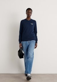 Marinegenser med rund hals, parret med lyseblå rette jeans. Svart håndveske i hånden, brukt med svarte sko og hvite sokker.