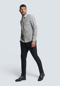 Graues Hemd mit Knopfleiste und subtilen Muster, kombiniert mit schwarzen, taillierten Hosen und schwarzen ankle boots. Taillierte Passform, lange Ärmel und Kragen.