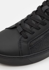 Czarne skórzane sneakersy z fakturowanym wykończeniem, płaskimi sznurówkami i akcentem zamka. Posiadają wytłoczone logo oraz gumową podeszwę.