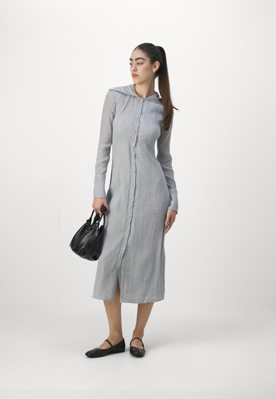 Light gray long dress with vertical stripes, button-down front, and hood. Model holds a black bag and wears flat black shoes.