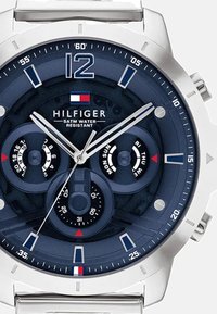 Montre bleu marine avec boîtier en acier inoxydable argenté, grand chiffre 12, plusieurs cadrans pour la date et la semaine, et un logo sur le cadran. Étanche jusqu'à 5 ATM.