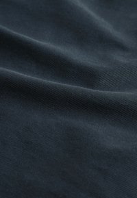 Tmavě modrá látka s jemným diagonálním žebrov�áním a měkkými záhyby, které zdůrazňují texturu a splývání.