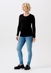 Svart långärmad gravidblus i kombination med ljusblå skinnyjeans och svarta platåskor. Slätt tyg och figurnära design.
