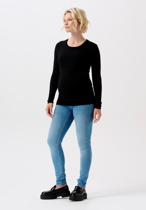Zwarte langdurige zwangerschaps top gecombineerd met lichtblauwe skinny jeans en zwarte platform schoenen. Soepele stof en aansluitend ontwerp.