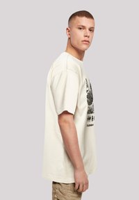 Cream-colored oversized t-shirt with short sleeves, featuring a black graphic print on the front and a relaxed fit.