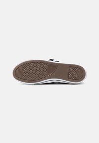 Sneaker nera con una suola in gomma marrone testurizzata, dotata di una intersuola bianca e un battistrada a motivo a diamante per una migliore aderenza.