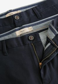 Tengerészi slim fit nadrág, cipzáras, gombos záródással és kockás anyagbéléssel. Barna varrással és díszítő részletekkel ellátva.
