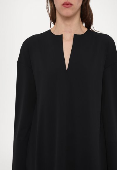 Crna tunika s širokim izrezom i malim prorezom, dugim rukavima i glatkim, laganim materijalom. Jednostavan i minimalistički dizajn.