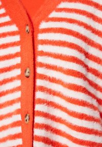 Oranžový texturovaný kardigan s bílými pruhy, s výstřihem do véčka a knoflíky ze dřeva, zdůrazňující měkký, plyšový materiál.