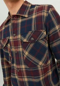 Camisa de franela a cuadros en navy, burdeos y beige. Diseño de botones con dos bolsillos en el pecho y un cuello clásico. Textura suave.