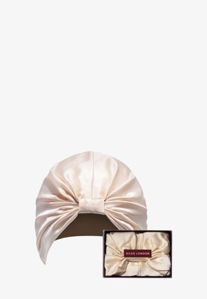 Bonnet de sommeil en satin de couleur crème douce avec un design de nœud à l'avant. Comprend une boîte assortie avec un branding rouge. Texture lisse, forme arrondie.