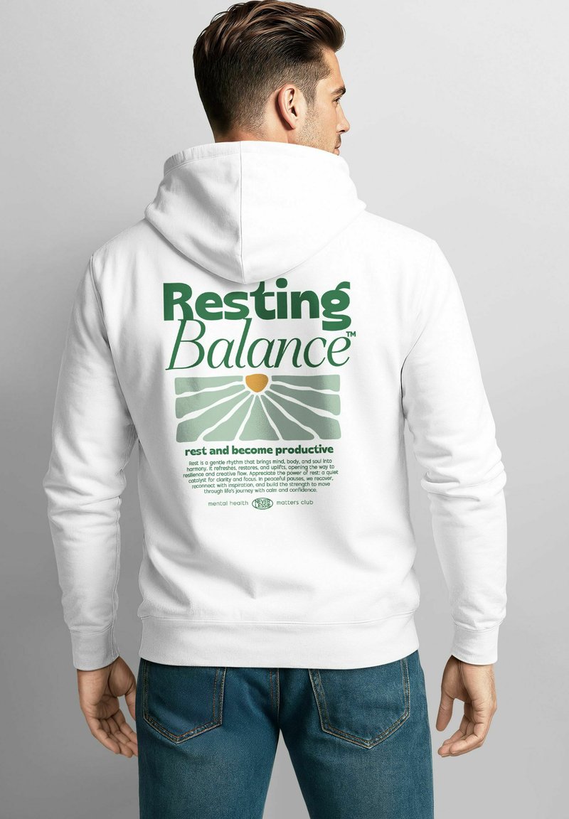 Mann trägt einen weißen Hoodie mit dem Schriftzug "Resting Balance" und einer grünen Grafik zur Förderung der psychischen Gesundheit auf dem Rücken, kombiniert mit blauen Jeans.