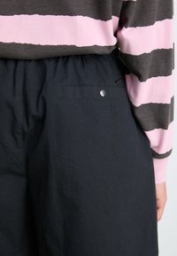 Black pants with an elastic waistband, featuring a sleek design and a rear pocket with a metal snap closure. Striped top in gray and pink.