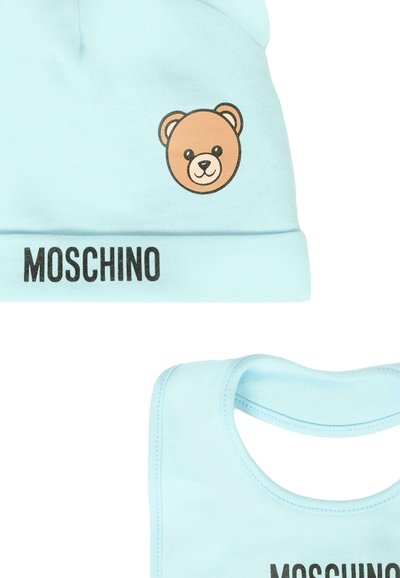 Cappello e bavaglino in cotone azzurro chiaro con una grafica di un orso bruno e il testo "MOSCHINO" in nero lungo il bordo inferiore. Texture liscia.