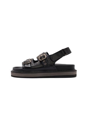 Sandal in pelle nera con due cinturini regolabili con fibbie, dettagli con borchie e una spessa suola piattaforma nera e beige.