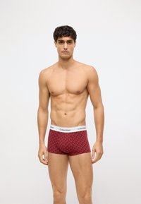 Czerwone bokserki w geometryczny wzór z białym pasem Calvin Klein. Materiał wydaje się gładki i elastyczny.