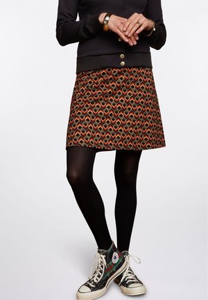 Une jupe à motifs géométriques dans des couleurs chaudes, associée à des collants noirs et des baskets Converse à carreaux.