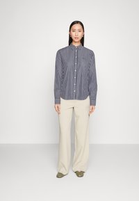Button-up shirt with vertical navy and white stripes, long sleeves, and a pointed collar, paired with cream wide-leg trousers and green shoes.