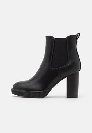 Bottine en cuir noir avec talon bloc, panneaux élastiques sur les côtés, semelle texturée et languette à l'arrière pour un enfilage facile.