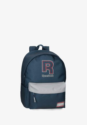 Mochila Reebok azul marino con gran logo "R" rojo y blanco, bolsillo frontal con cremallera gris y correas de hombro acolchadas.
