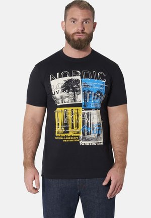 Bärtiger Mann, der ein schwarzes T-Shirt mit mehrfarbigem grafischem Text und Bildern trägt, steht mit neutralem Gesichtsausdruck vor einem weißen Hintergrund.