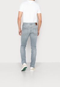 Vaqueros de color azul claro con un ajuste slim y un ligero desgaste, con bolsillos traseros y una etiqueta de cuero marrón en la cinturilla. Combinados con una camiseta blanca.