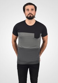 Černé a šedé tričko s krátkým rukávem, které má horizontální design barevných bloků a kapsu na hrudi. Měkká, hladká textura a slim fit.