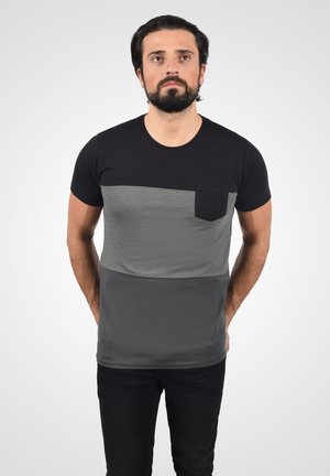 Camiseta de manga corta en negro y gris con un diseño de bloques de color horizontal y un bolsillo en el pecho. Textura suave y lisa con un corte ajustado.