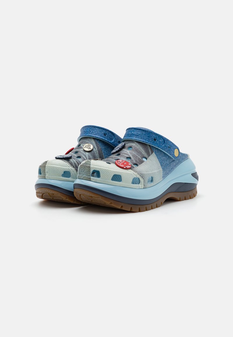 Zuecos azules y aqua con un acabado texturizado, que cuentan con orificios de ventilación, una correa de denim y pines decorativos. Suela de goma marrón.