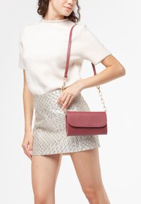 Borsa a tracolla bordeaux con una finitura texture, hardware dorato e una tracolla a catena. Indossata con una mini gonna argento a fantasia.