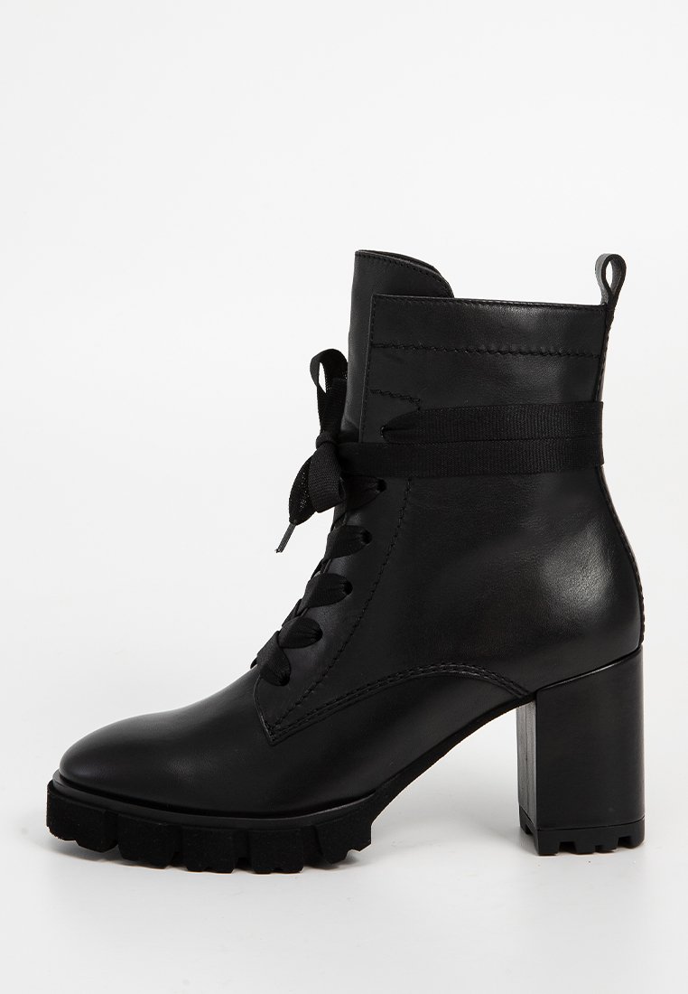 Bottine en cuir noir avec un bout rond, système de laçage à l'avant, talon large et bloc, et semelle en caoutchouc pour une meilleure adhérence. Dotée d'une sangle en tissu à la cheville.