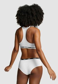 Weißer Sport-BH mit Racerback-Design und schwarzem Puma-Logo-Band; passende weiße High-Waist-Unterwäsche mit schwarzem Bund.
