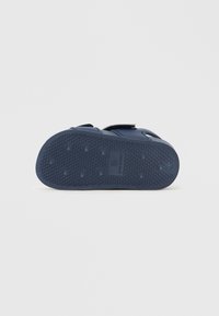 Suela de sandalia de goma azul con agarre texturizado, que incluye orificios de ventilación y una correa de velcro. Material duradero, diseño ligero.