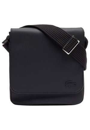 Bolso negro rectangular bandolera con superficie texturizada, correa ancha ajustable y logo de cocodrilo en relieve en la esquina inferior derecha.