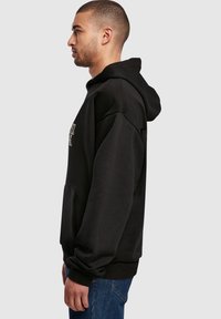 Schwarzer Kapuzenpullover mit lockerer Passform, mit einer Fronttasche, gerippten Manschetten und weichem, strukturiertem Stoff.