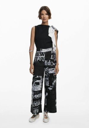 Black sleeveless top with a white accent scarf; wide-leg pants featuring a black and white graphic text design; casual footwear.