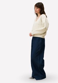 Pull en maille couleur crème avec un col en V, associé à un pantalon large en velours côtelé bleu foncé. La tenue présente une texture subtile et un volume équilibré.