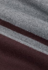 Wełniany koc w szare i ciemno-brązowe paski. Miękka tekstura z gładkim wykończeniem i subtelnym wzorem splotu.