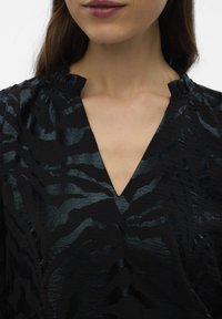 Zwart topje met een gestructureerde stof met een subtiele glans, V-hals ontwerp en een geplooid detail bij de halslijn, met een golfpatroon.