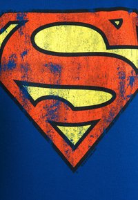Blue T-shirt featuring a distressed red and yellow Superman logo centered on the chest, with a smooth, cotton texture.