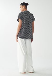 Zwart-wit gemusterde blouse met korte mouwen en kraag, gecombineerd met witte wijde broek. Glad stof en een ontspannen silhouet.