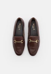 Καφέ δερμάτινες λόφερς με χρυσή λεπτομέρεια, που διαθέτουν λεία υφή και στρογγυλή μύτη. Στο εσωτερικό εμφανίζεται το όνομα της μάρκας σε χρυσό.