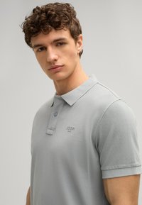 Grijze polo shirt gemaakt van textuurstof, met een klassieke kraag en twee knopen, en een subtiel geborduurd logo op de borst.