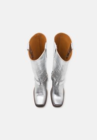Bottes argentées mi-mollet en matériau métallique. Bout carré, texture lisse, intérieur contrastant en tan, et accents décoratifs sur les côtés.