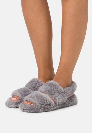 Chaussons en peluche gris avec deux larges bandes, ouverte à l'avant et texture douce. Design simple adapté pour une utilisation intérieure.